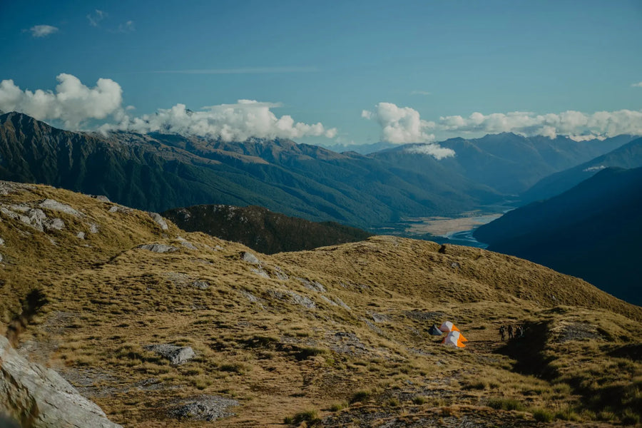 Two people standing on a mountain top with a scenic view of mountains and clouds.